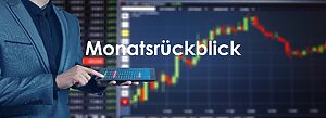 Person in Anzug hält ein Tablet mit Marktübersicht, im Hintergrund unscharfe Finanzcharts mit steigenden und fallenden Kursen sowie dem Wort „Monatsrückblick“ zentral im Bild.
